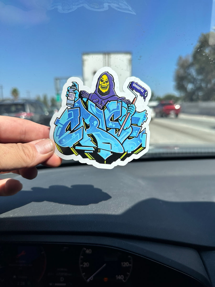 Hand holding a printed graffiti sticker with a white border around the artwork
